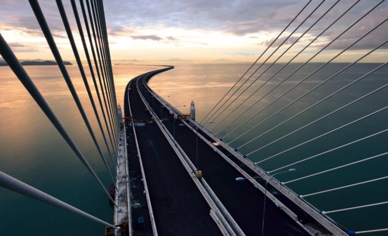 Long road and suspension bridge over calm water